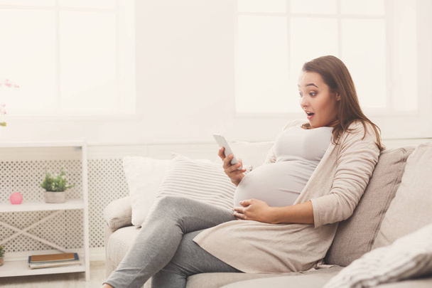 Meglepett a terhes nő használ smartphone otthon - Fotó, kép