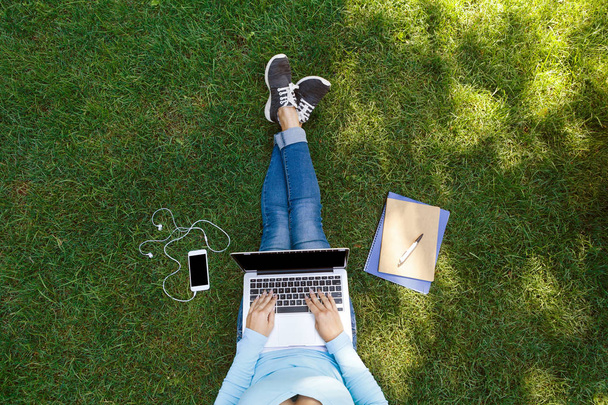 Visão superior de estudante do sexo feminino sentado no parque com laptop
 - Foto, Imagem