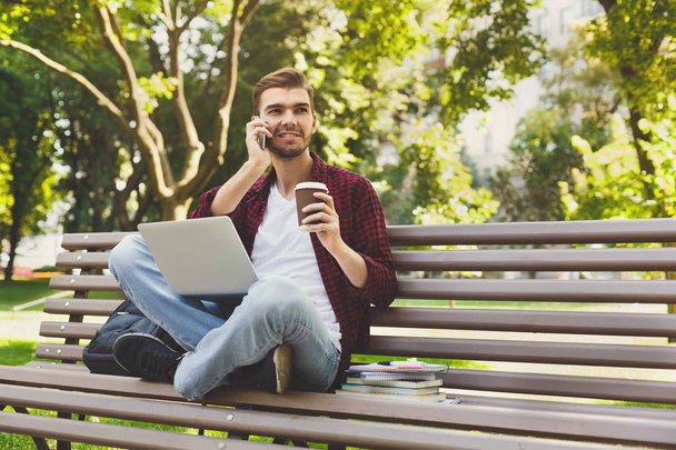 Man with laptop, talking on the smartphone outdoors - Photo, Image