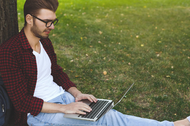 Homme concentré avec ordinateur portable travaillant sous un arbre à l'extérieur
 - Photo, image