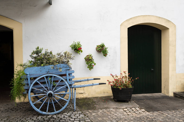 Old fashioned cart for horse with flowers by old white wall - Photo, Image