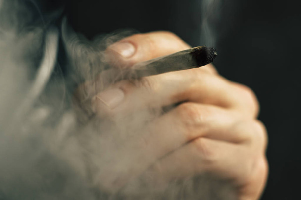 Человек курит марихуану косяк и зажигалку в руках. Дым на черном фоне. Концепции использования медицинской марихуаны и легализации марихуаны
. - Фото, изображение