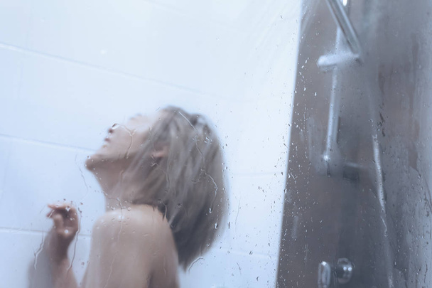 Donna sta lavando nella vasca da bagno doccia attraverso la superficie di vetro wi
 - Foto, immagini