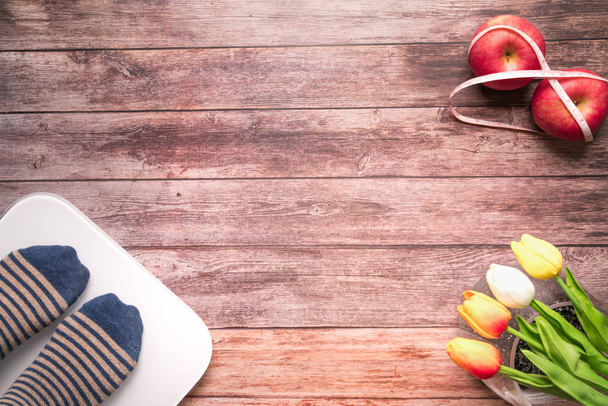 βάρος ψηφιακή κλίμακα λευκό με γυναικών πόδια καθώς στέκεται όρθιος στην κλίμακα και διατροφή δεσμεύουν κόκκινο μήλο με μεζούρα ξύλινο υπόβαθρο στην υγεία και fitness ζωή έννοια - Φωτογραφία, εικόνα
