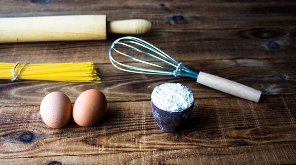 спагетти, мука и яйца с посудой на деревянном фоне
 - Фото, изображение