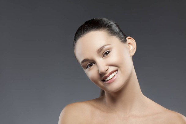 Portrait of young smiling woman with natural makeup against grey background - Fotó, kép