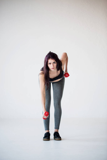 Serious sportwoman is doing hand exercises with dumbbells in the studio. Full-length front view. - Foto, Imagem