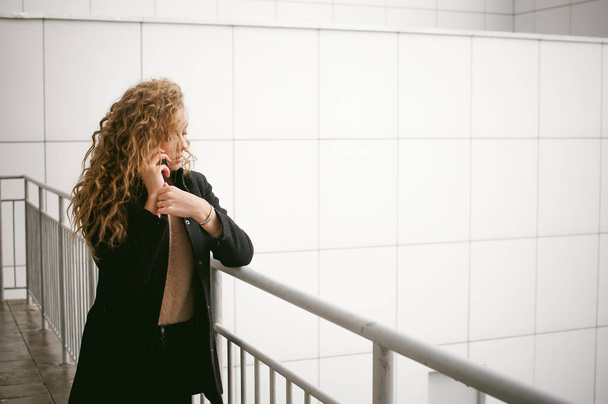 city portrait of a young woman with curly hair dressed in a black coat - 写真・画像