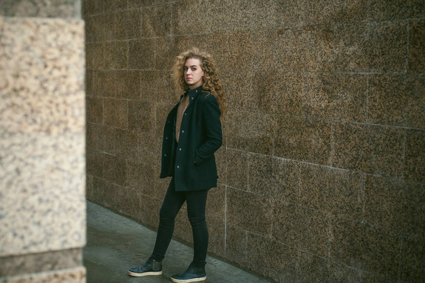 city portrait of a young woman with curly hair dressed in a black coat - Фото, изображение
