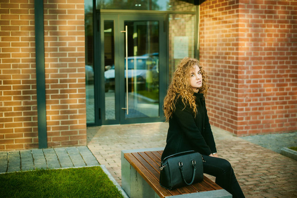 city portrait of a young woman with curly hair dressed in a black coat - Foto, afbeelding