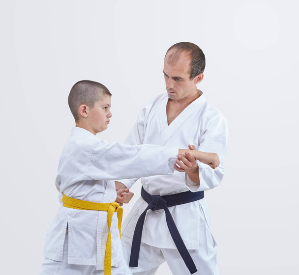 The trainer with black belt teaches karateka boy with yellow belt to beat the blow - Photo, Image