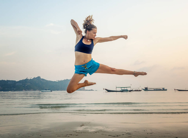 Beautiful sporty girl jumping on the beach against the sea - Fotografie, Obrázek