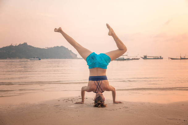 Młoda kobieta acrobat stoi na głowie, na piaszczystej plaży na b - Zdjęcie, obraz