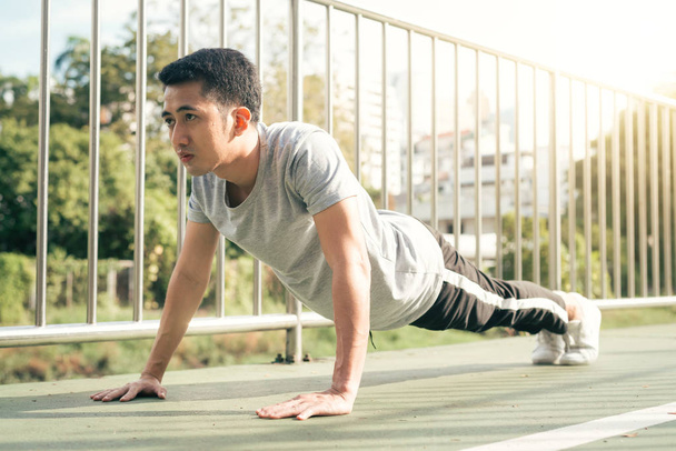 Fitness sport men fashion sportswear doing yoga fitness exercise in street. Fit young asian man doing training workout in morning. Young happy asian man stretching at park after running workout. - Photo, Image