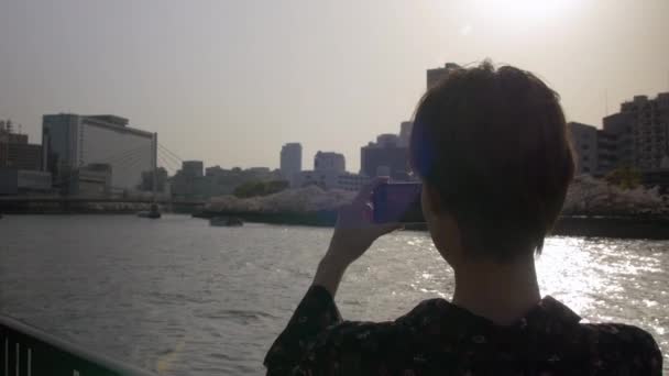 Young Japanese woman taking photos of sakura and river. - Metraje, vídeo