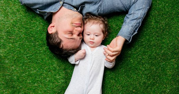 Молодые отец и сын лежат на зеленой траве
. - Фото, изображение