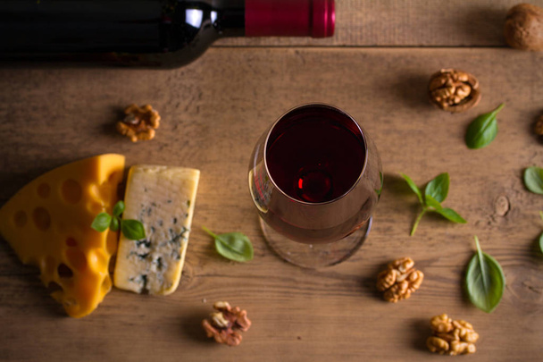 Red wine and cheese on wooden table background. Cheese appetizer selection or wine snack set. Glass and bottle of wine. overhead - Fotó, kép