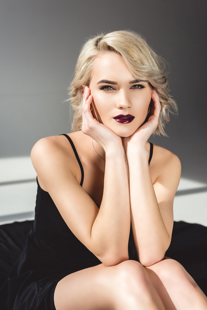 stylish blonde girl with makeup posing in black dress, on grey   - Zdjęcie, obraz