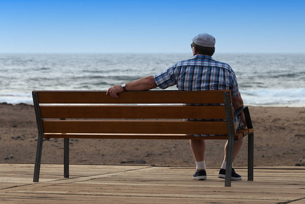 Pensioner sitting on a bench and looking at ocean - Foto, Imagen