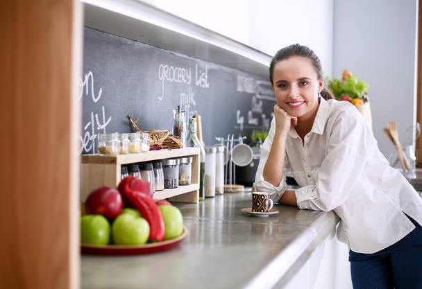 Portrait of young woman standing against kitchen background. - Photo, Image