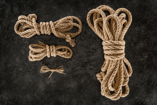 top view of arrangement of tied brown marine ropes on dark concrete surface - Foto, immagini