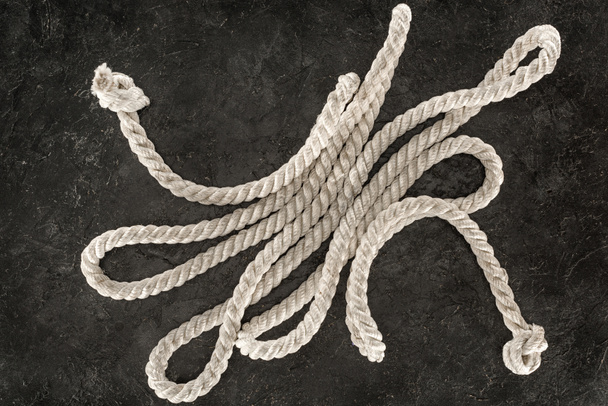 bovenaanzicht van witte nautische touw met knopen op donkere betonnen tafelblad - Foto, afbeelding