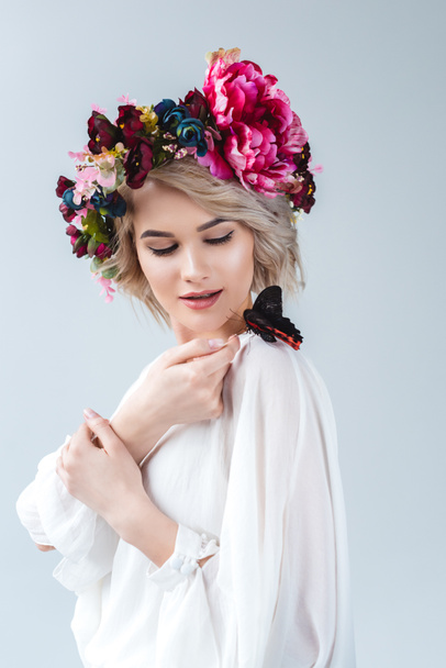 modelo atractivo posando en corona floral con mariposa en el hombro, aislado en gris
 - Foto, Imagen
