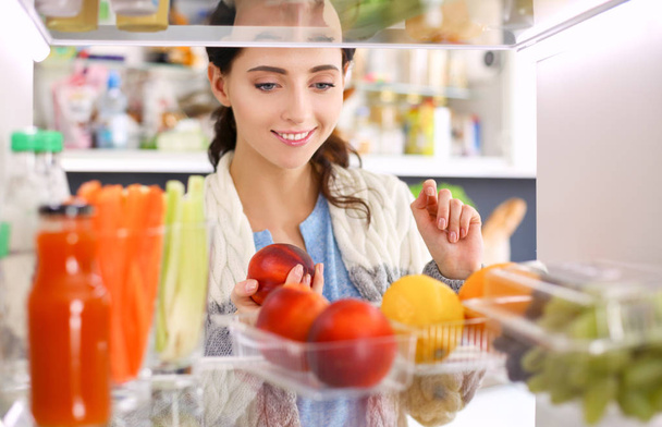 Retrato de fêmea em pé perto da geladeira aberta cheia de alimentos saudáveis, legumes e frutas. Retrato de fêmea - Foto, Imagem