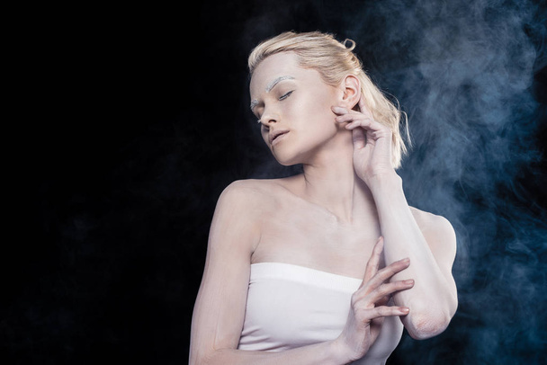 ελκυστική κοπέλα διαγωνισμού με κλειστά τα μάτια και λευκό μακιγιάζ, απομονώνονται σε μαύρο χρώμα με καπνό - Φωτογραφία, εικόνα
