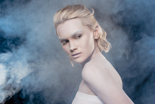 beautiful blonde girl with white makeup posing for fashion shoot in smoky studio - Фото, зображення