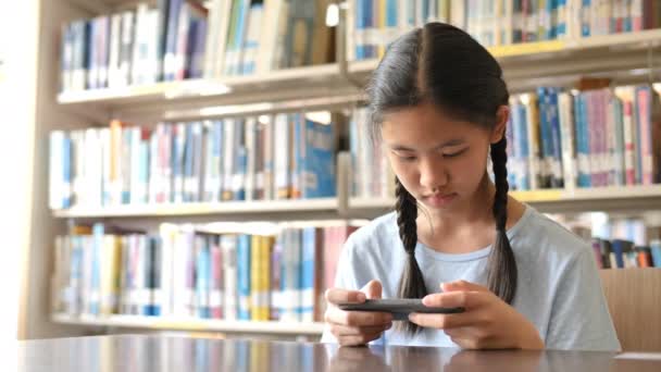 4 k Aziatische student met behulp van slimme telefoon in de schoolbibliotheek voor inspiratie, schiet met natuurlijk licht, Slow motion - Video