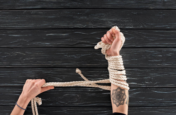 partial view of female hands with rope around on dark wooden tabletop - Photo, Image