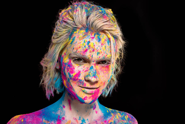 portrait of smiling girl in colorful holi paint, isolated on black - Foto, immagini