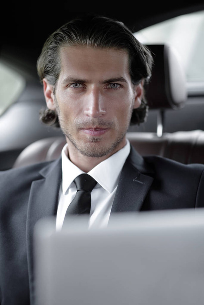 man sitting in the back-seat of a car, using his laptop - 写真・画像