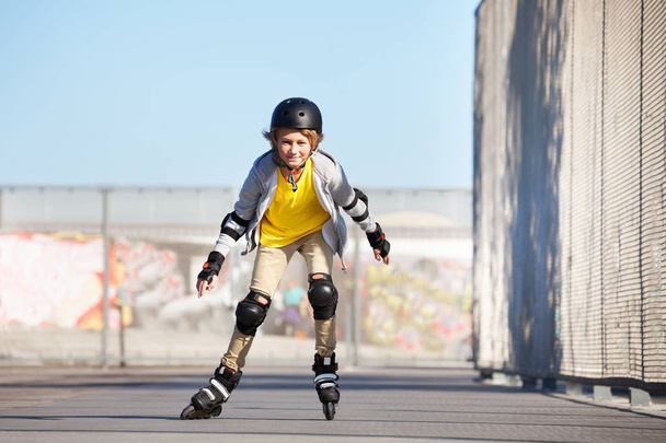 Portrait of smiling preteen boy on roller skates riding fast in skatepark - 写真・画像