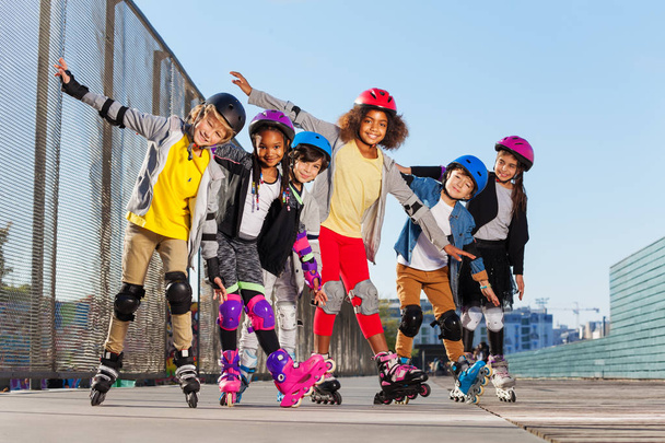Multiethnic boys and girls, happy sporty inline skaters, standing together in line with hands like wings outdoors - Foto, immagini