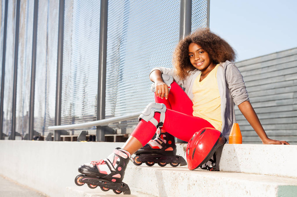 Happy African girl sitting on the stairs in roller skates at rollerdrom - Foto, imagen