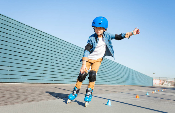 Preteen boy wearing protective gear, learning to roller skate on the road with cones - Foto, Imagen