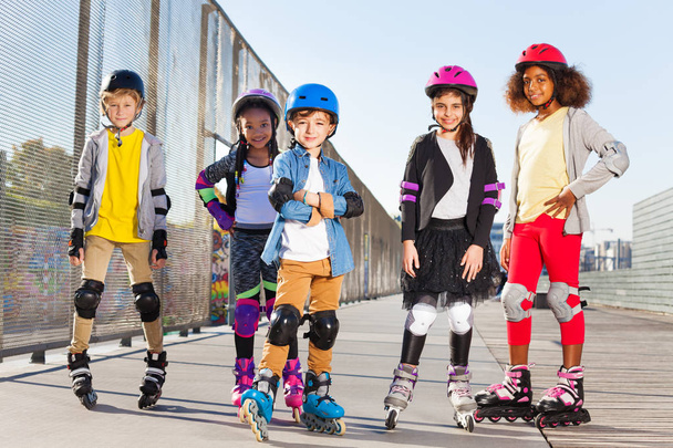 Happy schoolboy in roller helmet rollerblading with friends at stadium outdoors - Foto, Bild