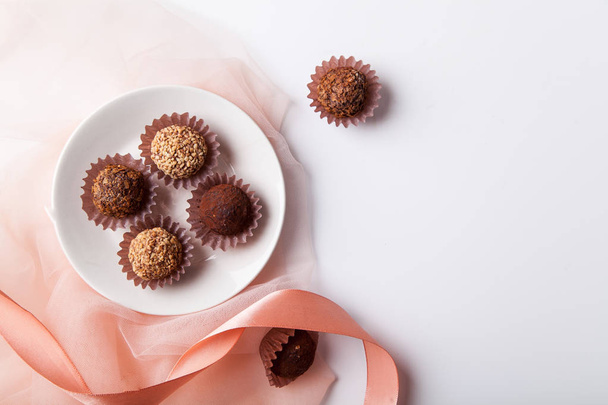 plate with variety of chocolate truffles and pink silk ribbon with transparent fabric on white background  - Φωτογραφία, εικόνα