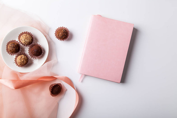 plate with variety of chocolate truffles and notebook on white background  - Фото, изображение