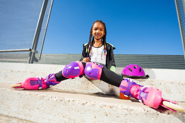 Portrait of African roller girl resting on the steps of skate park at sunny day - Фото, изображение