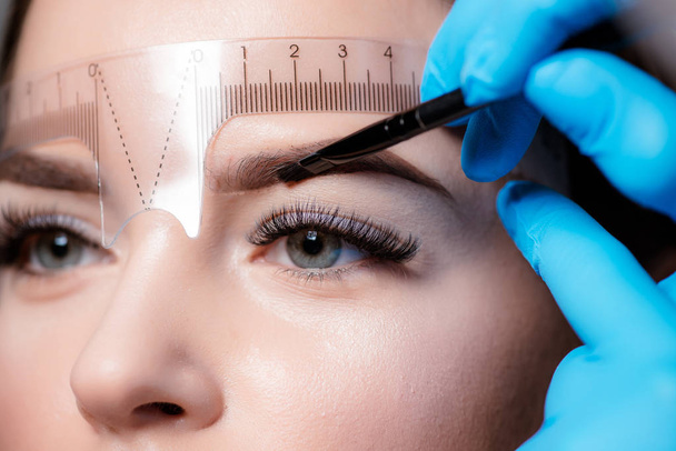 Young woman undergoing eyebrow correction procedure on light background - Foto, Imagem