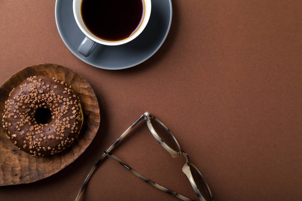 csokoládés fánk és csésze fekete kávé barna háttér, monokróm koncepció napszemüveg  - Fotó, kép