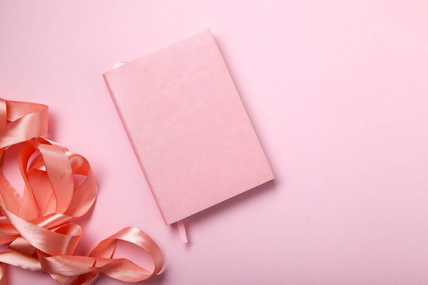 pink notebook with shiny pink satin ribbon on pink background, monochromatic concept  - Photo, image