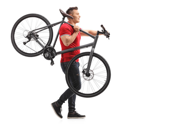 Full length profile shot of a young man carrying a bicycle on his shoulder isolated on white background - Photo, Image
