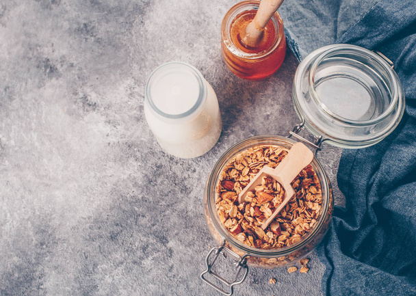 Homemade granola in glass jar on gray stone table. Ingredients for healthy breakfast - granola, milk or yogurt and honey. Top view, Copy space for text. - Fotó, kép