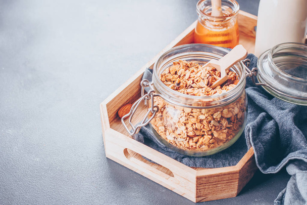 Ingredients for healthy breakfast - granola, milk or yogurt and honey. Granola in glass jar on wooden tray. Copy space for text. - Foto, imagen