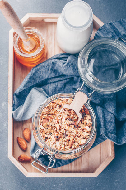 健康的な朝食のグラノーラ、牛乳またはヨーグルト、石のテーブル背景に木製のトレイの上に蜂蜜。上面図、クローズ アップ - 写真・画像