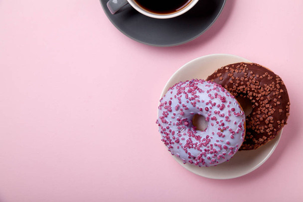 chocolate donuts on plate with cup of black coffee on pink background, close-up  - Photo, Image